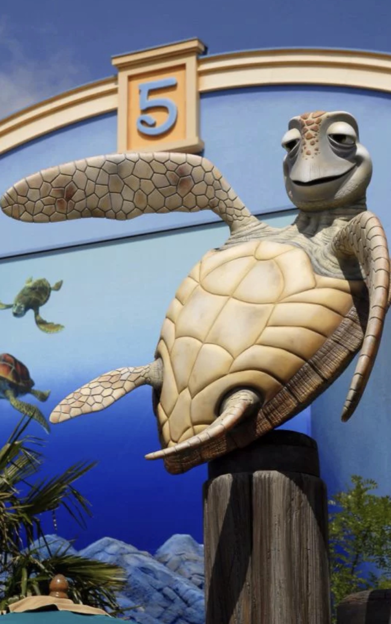 Estatua de Crush sobre el cartel número 5 de la cola virtual de Crush's Coaster en Disney Adventure World